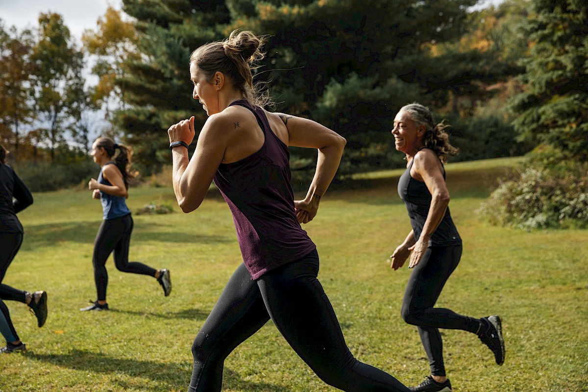 A group of people are running outdoors on a grassy area, surrounded by trees and autumn foliage.