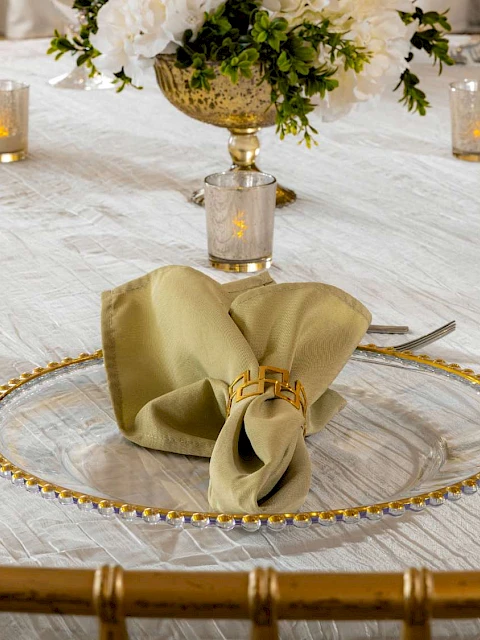 A table elegantly set with a gold-rimmed plate, folded napkin, silverware, wine glasses, and floral centerpiece on a white tablecloth.