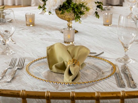 A formal dining table set with fine glassware, silverware, a decorative plate, green napkin, flowers, and candles on a white tablecloth.