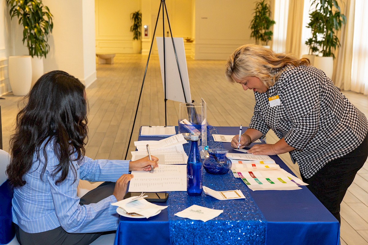 Two people are engaged in paperwork at a blue-clothed table, possibly during an event registration or check-in process.
