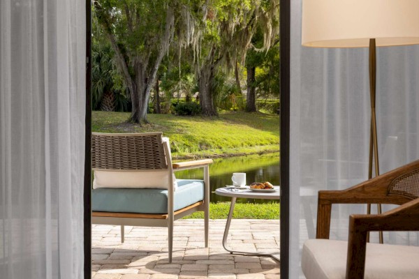 A cozy indoor seating area by a glass door leading to an outdoor patio with chairs, table, and a view of greenery and water beyond.