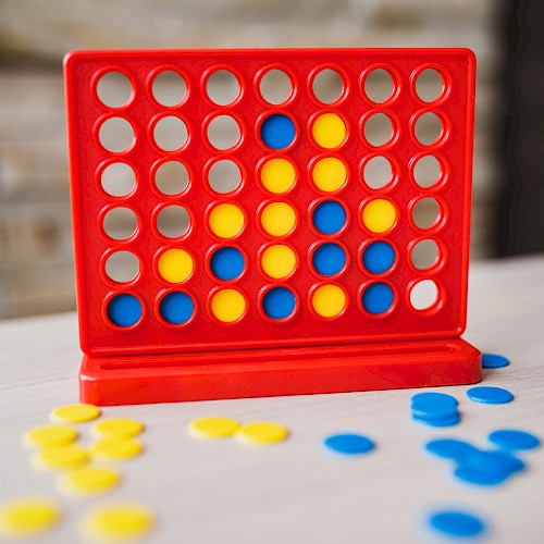 A Connect Four game in progress with blue and yellow discs on a table, featuring a red vertical grid.