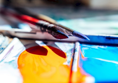 Paintbrushes resting on a palette with vibrant orange and blue paint, capturing an artistic scene.