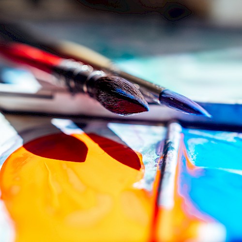 Paintbrushes resting on a palette with vibrant orange and blue paint, capturing an artistic scene.