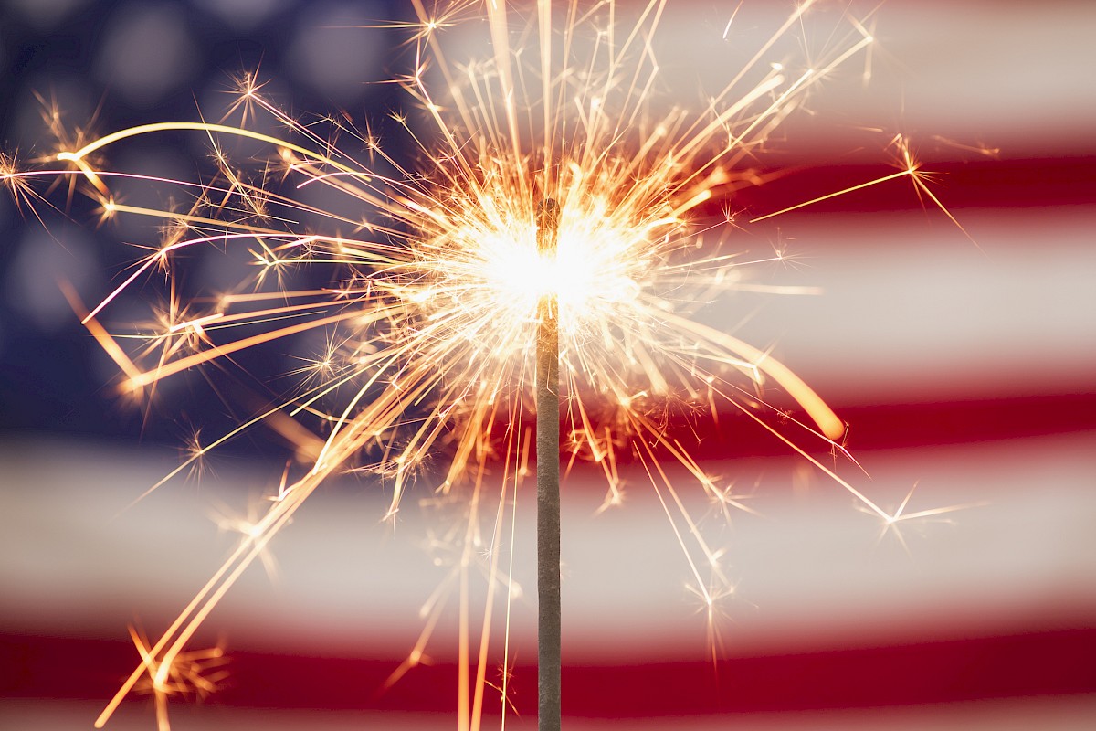A sparkler in front of an American flag, celebrating Independence Day with fireworks and patriotism.