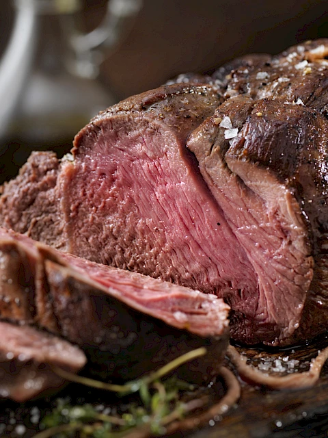 A juicy, perfectly seared steak, pink and tender in the center, sliced on a dark board with herbs for garnish.