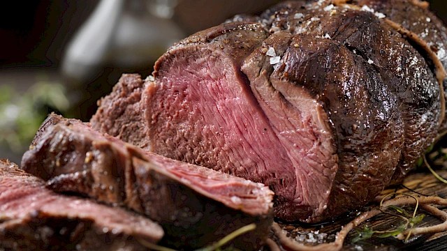 A juicy, perfectly seared steak, pink and tender in the center, sliced on a dark board with herbs for garnish.