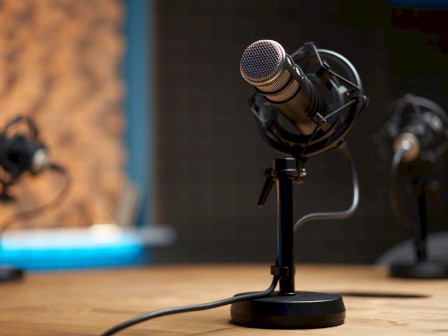 A close-up of a microphone on a desk with more in the background, set in a recording studio environment.