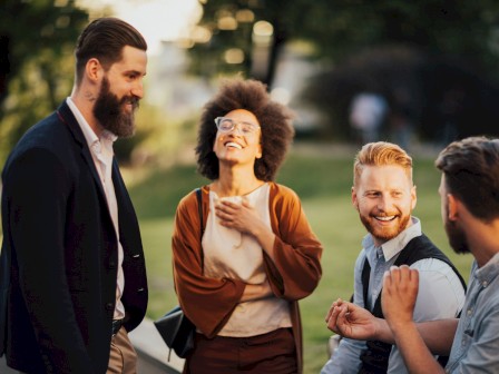 A group of four people are outdoors, dressed in business casual attire, engaging in a cheerful conversation.
