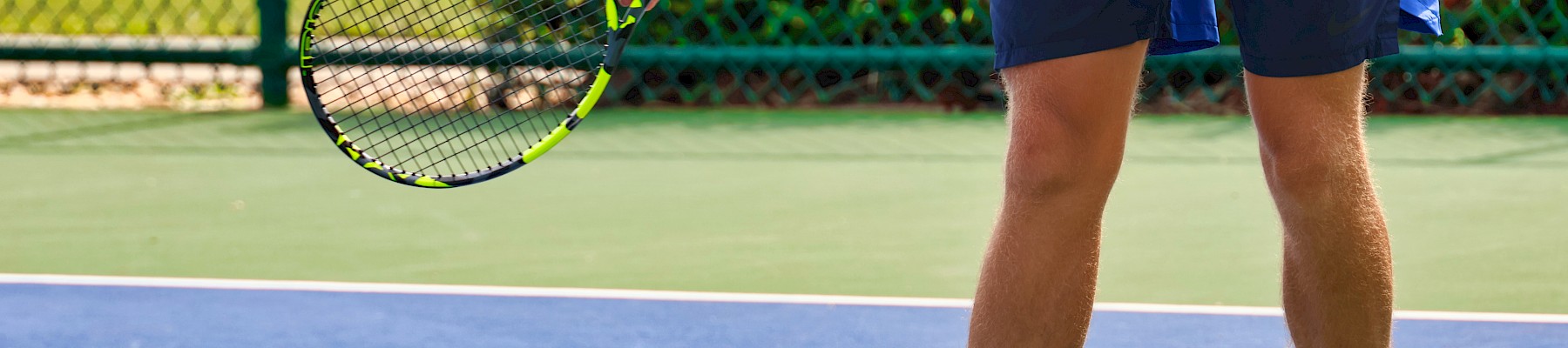 A person is preparing to serve on a tennis court, holding a racquet and wearing sports clothes and shoes.
