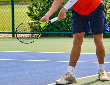 A person is preparing to serve on a tennis court, holding a racquet and wearing sports clothes and shoes.