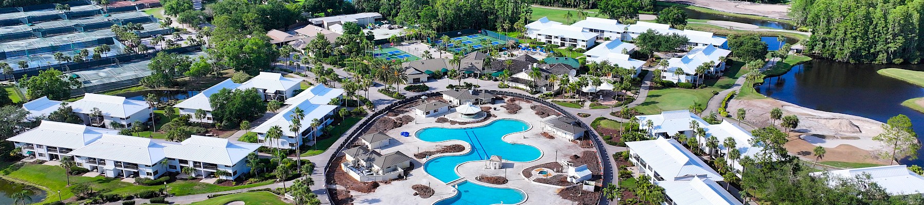 The image shows an aerial view of a resort with a large pool, surrounded by greenery, buildings, and a golf course.