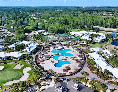 The image shows an aerial view of a resort with a large pool, surrounded by greenery, buildings, and a golf course.