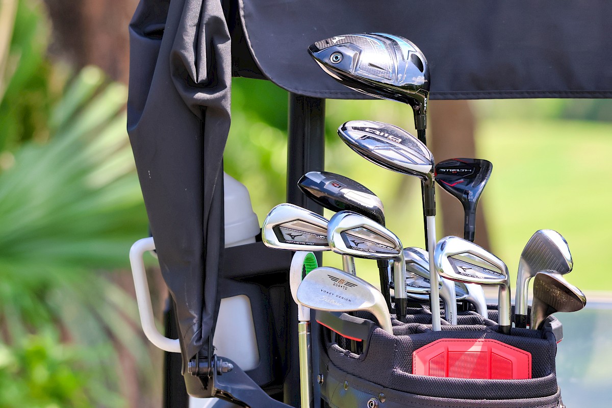 A set of golf clubs in a bag on a golf course, with trees and greenery in the background.