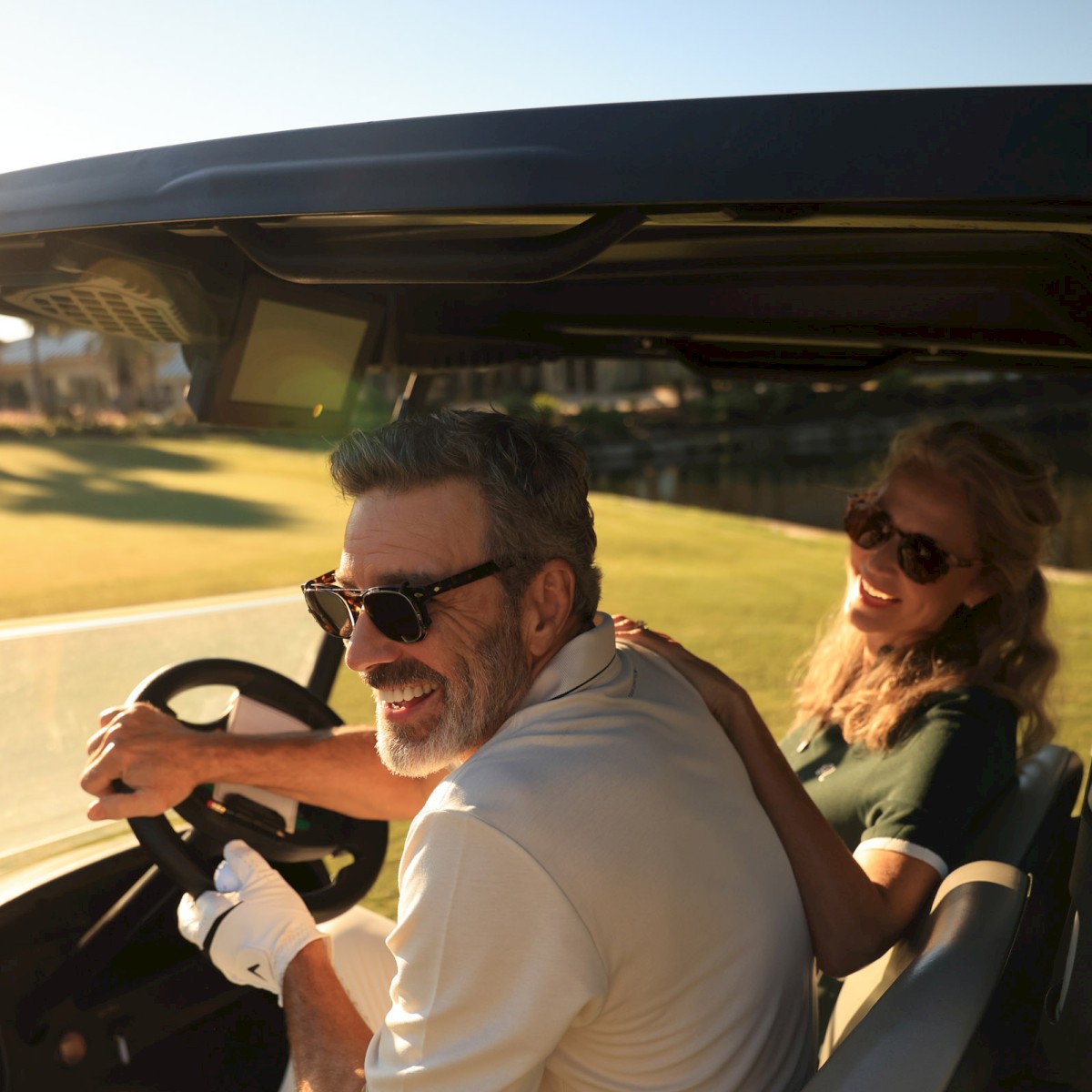 A happy man and woman enjoy a golf cart ride together outdoors during sunset.