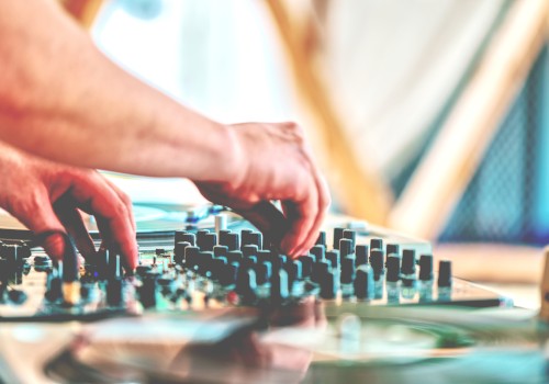 A person adjusting a DJ mixer or audio mixer with multiple knobs and sliders on a table, in a studio setup.