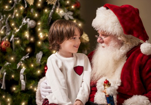 A child sits on Santa's lap by a decorated Christmas tree, sharing a joyful moment.