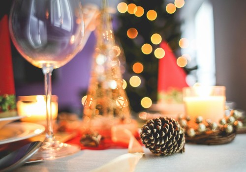 A festive table with a pinecone centerpiece, candles, blurred fairy lights, wine glass, and holiday decorations in the background.