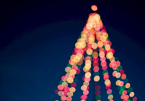 A blurry festive Christmas tree made of colorful lights, glowing against a dark blue sky, with a bright top light.