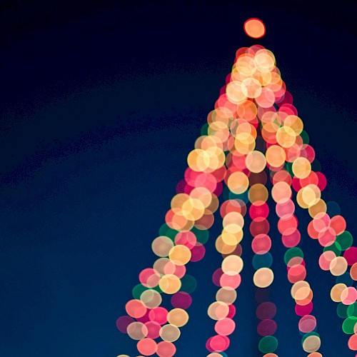 A blurry festive Christmas tree made of colorful lights, glowing against a dark blue sky, with a bright top light.