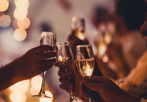 A group toasts with champagne flutes at a warmly lit celebration, clinking glasses as blurred festive lights glow in the background.