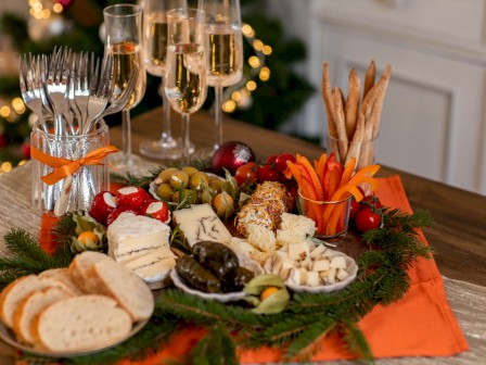 A festive charcuterie board with bread, cheeses, grapes, olives, nuts, veggies, dips, and breadsticks, plus champagne flutes in a cozy setting.