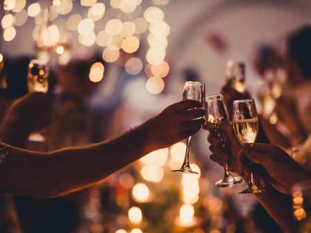 People at a party clinking champagne flutes in a celebratory toast, warm lights and blurred background creating a festive atmosphere.