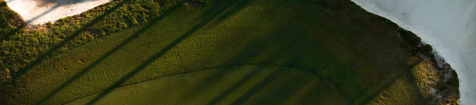 A snowy landscape with a dark green pond or puddle at the bottom, casting long shadows from nearby trees across the icy surface.
