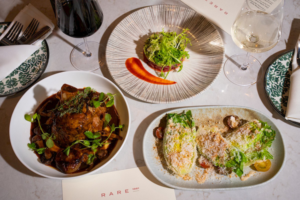 A stylish restaurant spread with three plated dishes and wine glasses on a pale table, ready for a meal.