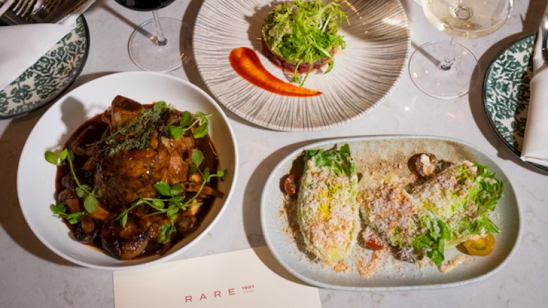 A stylish restaurant spread with three plated dishes and wine glasses on a pale table, ready for a meal.