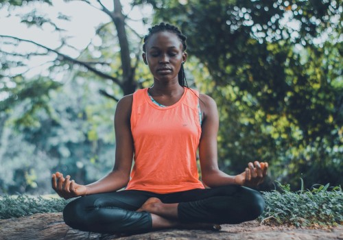 A woman is practicing meditation or yoga outdoors on a log surrounded by trees and greenery.