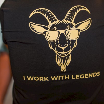 A person is wearing a black shirt with a goat wearing sunglasses and the text 