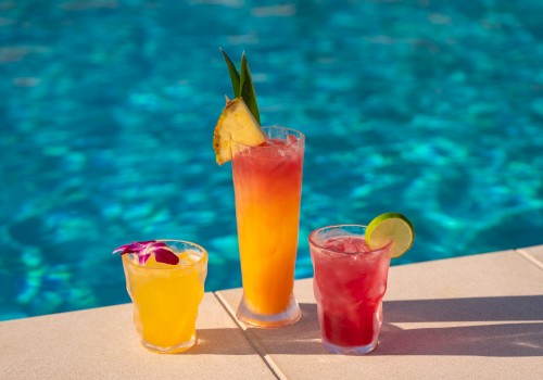 Colorful tropical cocktails with fruit garnishes are set beside a swimming pool, creating a perfect summer poolside scene.