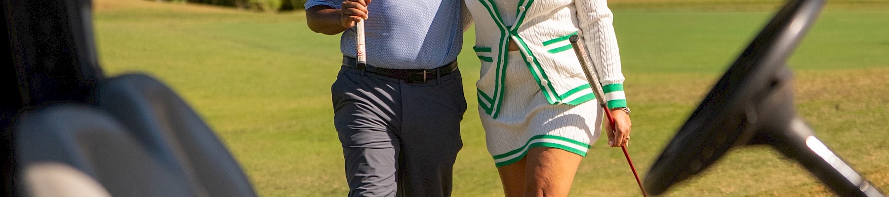 Two people smiling and walking on a golf course, holding golf clubs and enjoying each other's company.