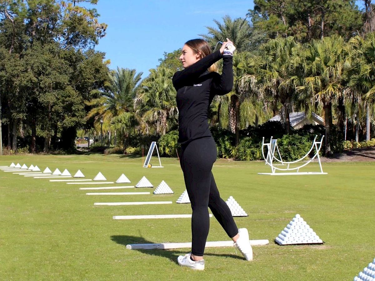 A person swinging a golf club on a driving range with pyramids of golf balls