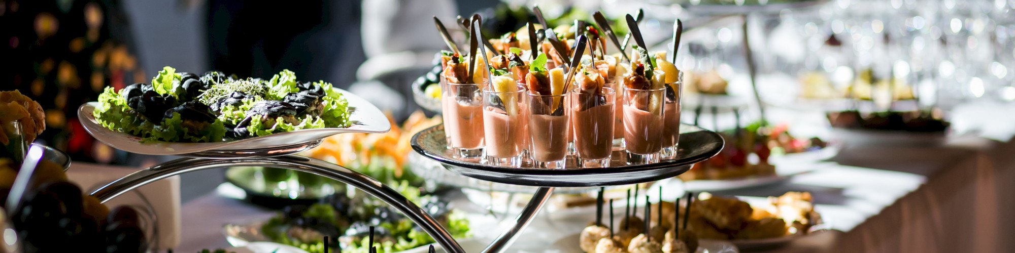 A buffet table with a variety of appetizers, pastries, and drinks set on different tiers under bright lighting.