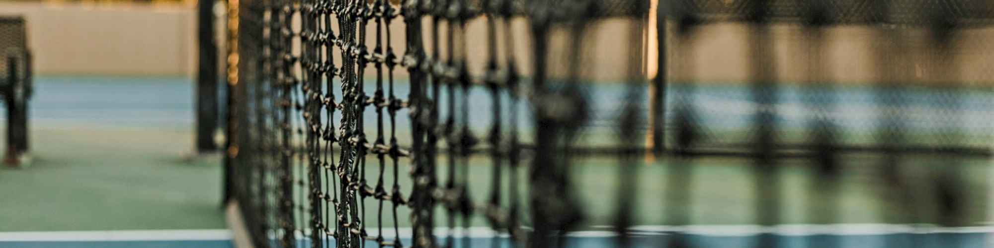 The image shows a close-up of a tennis net on a court with the background softly blurred, highlighting the net's details.