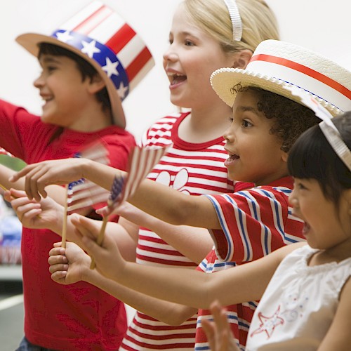 Kids celebrating at an outdoor event with patriotic hats, flags, and red, white, and blue clothing, likely for Independence Day.