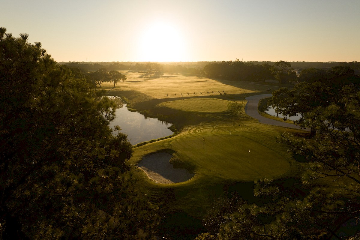 A scenic view of a golf course at sunset with trees, water hazards, and a winding cart path.