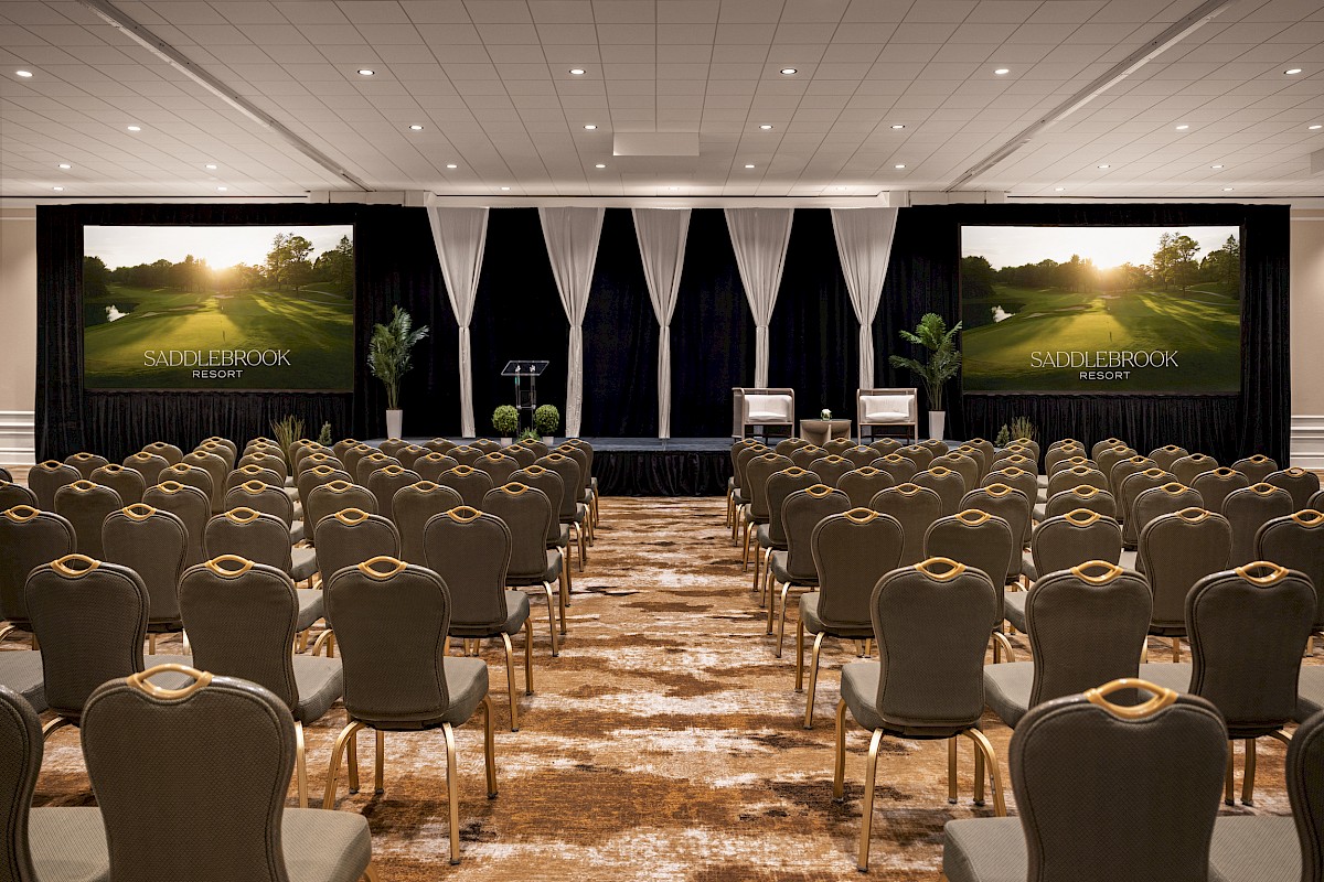 A conference room with chairs facing a stage, large screens showing 