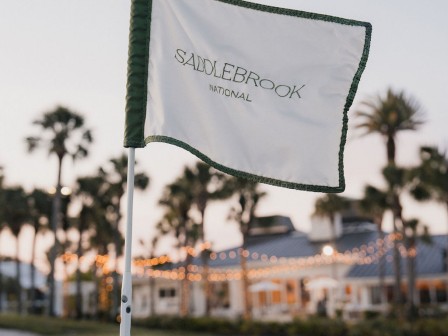 A flag at Saddlebrook National Golf Course with palm trees and clubhouse lights in the background at sunset.