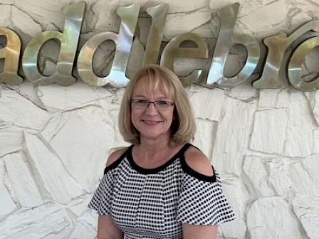A woman with glasses in front of a wall with a metallic 