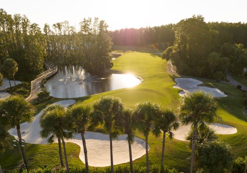 A golf course with sand traps, water hazards, and palm trees is illuminated by the setting sun.