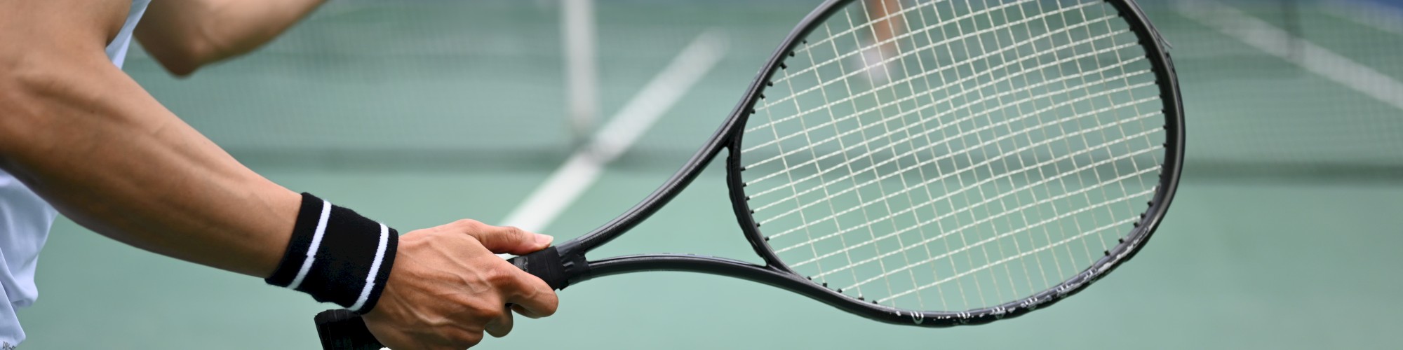 A person prepares to serve a tennis ball on a court, holding a racket, with a net and opponent visible in the background.