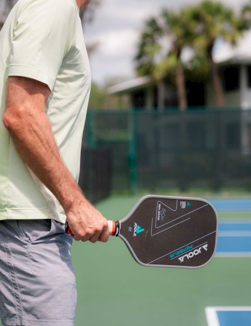 A person holding a pickleball paddle stands on a court, ready to play.