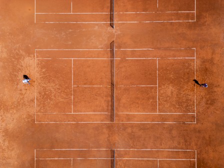 The image shows an aerial view of two players on a clay tennis court during a match.