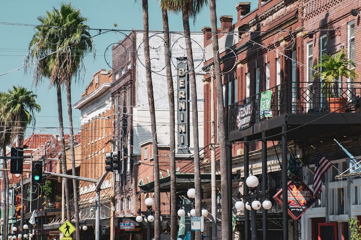 A street view with palm trees, historic brick buildings, and various storefronts, including a sign for 