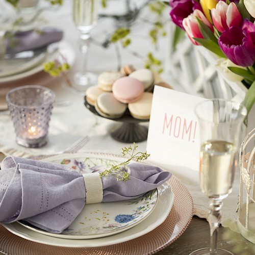 A beautifully set table with purple napkins, flowers, macarons, a 
