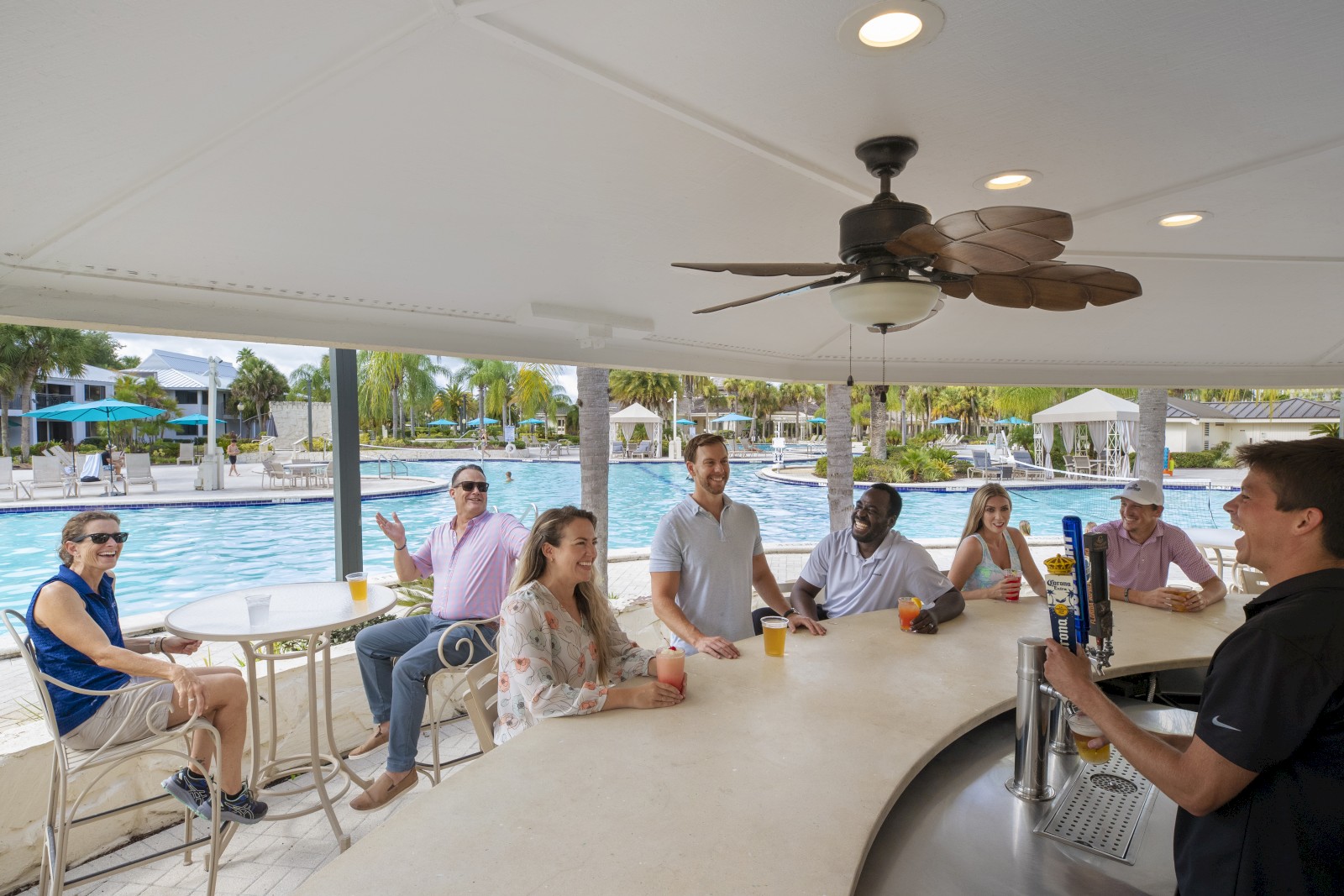 People sitting at a poolside bar with drinks, talking to a bartender.