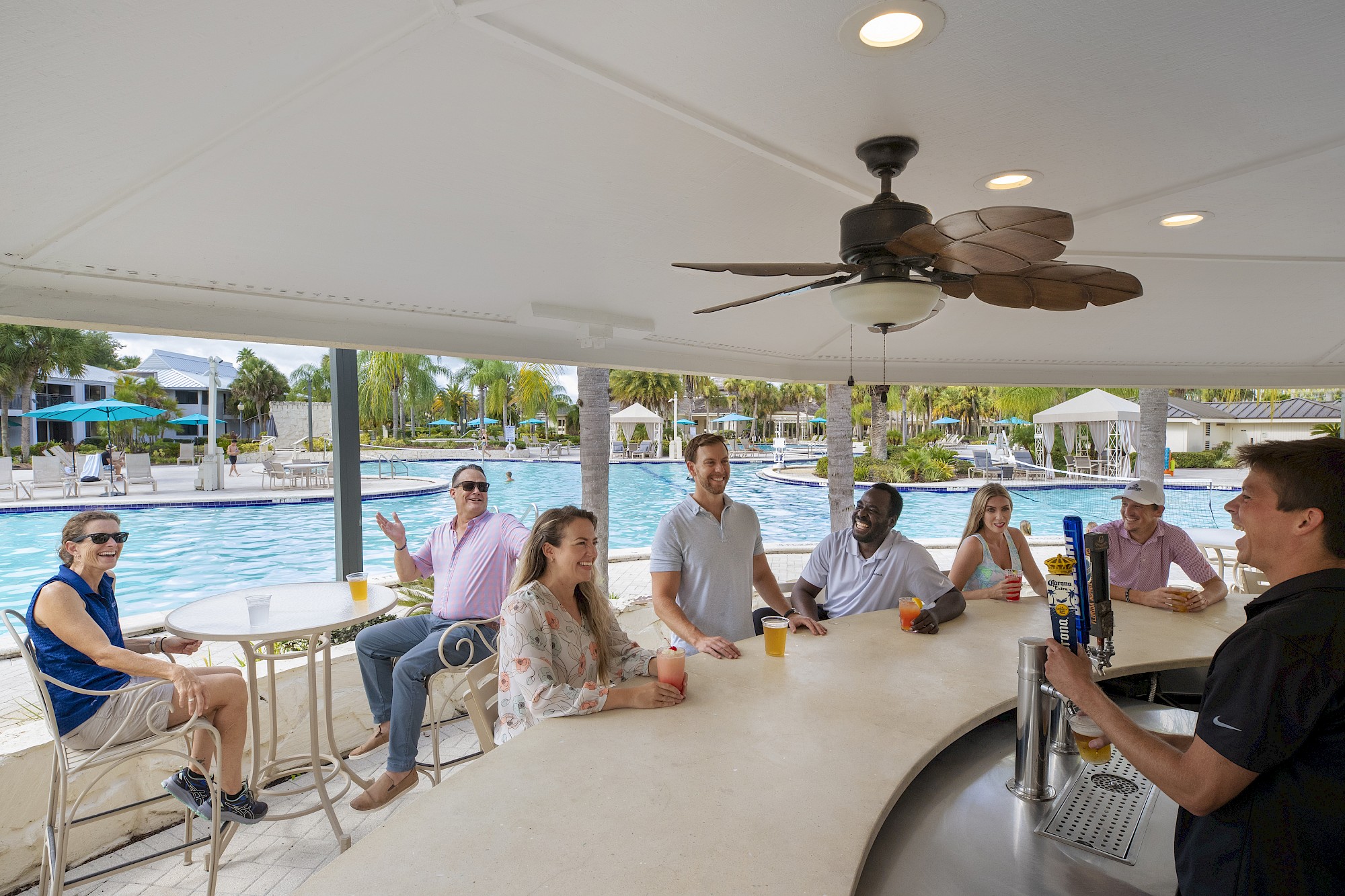 People sitting at a poolside bar with drinks, talking to a bartender.